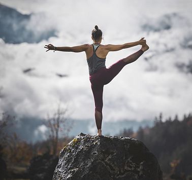 Frau steht auf Stein und führt anspruchsvolle Yogaposition durch