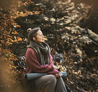 Frau sitzt mit Yogamatte im herbstlichen Laubwald